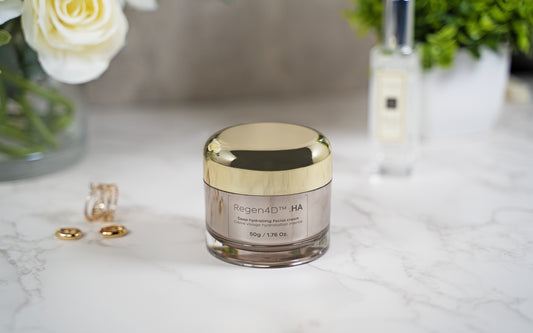 Regen4D® face cream displayed next to elegant jewelry and delicate white flowers, with a lush green shrub in the background.